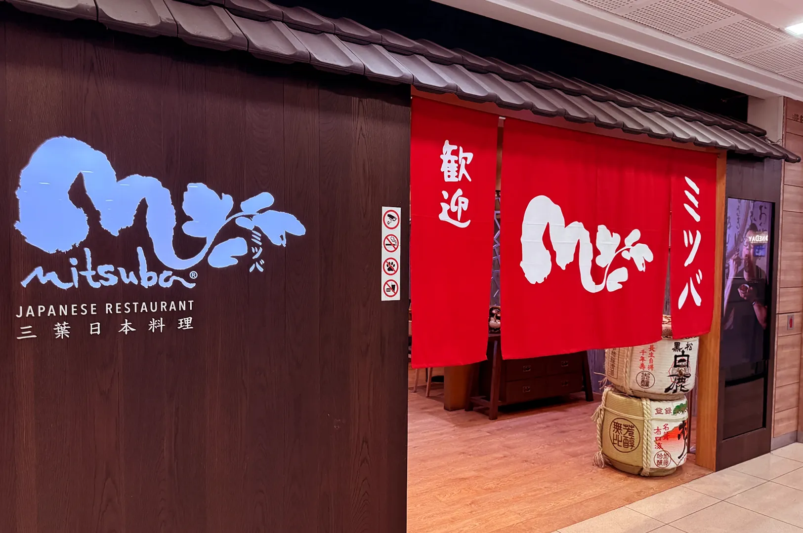 Mitsuba Japanese Restaurant entrance with a red noren curtain, dark wood facade, and Japanese signage.