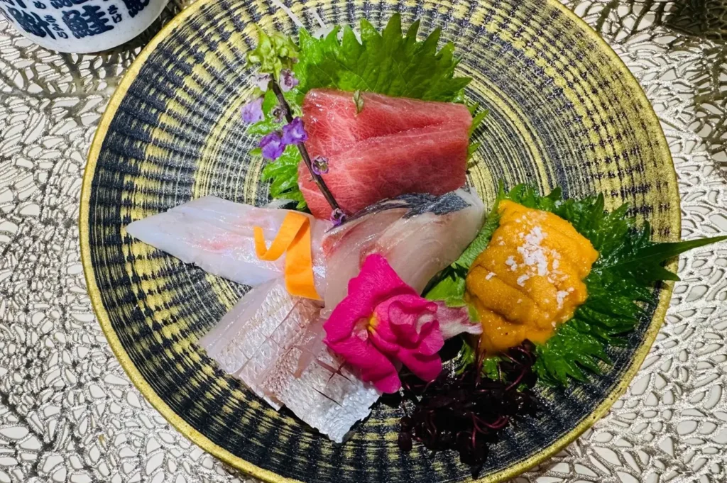 Omakase course with small dishes and glassware arranged inside a circular black metal frame on a counter.