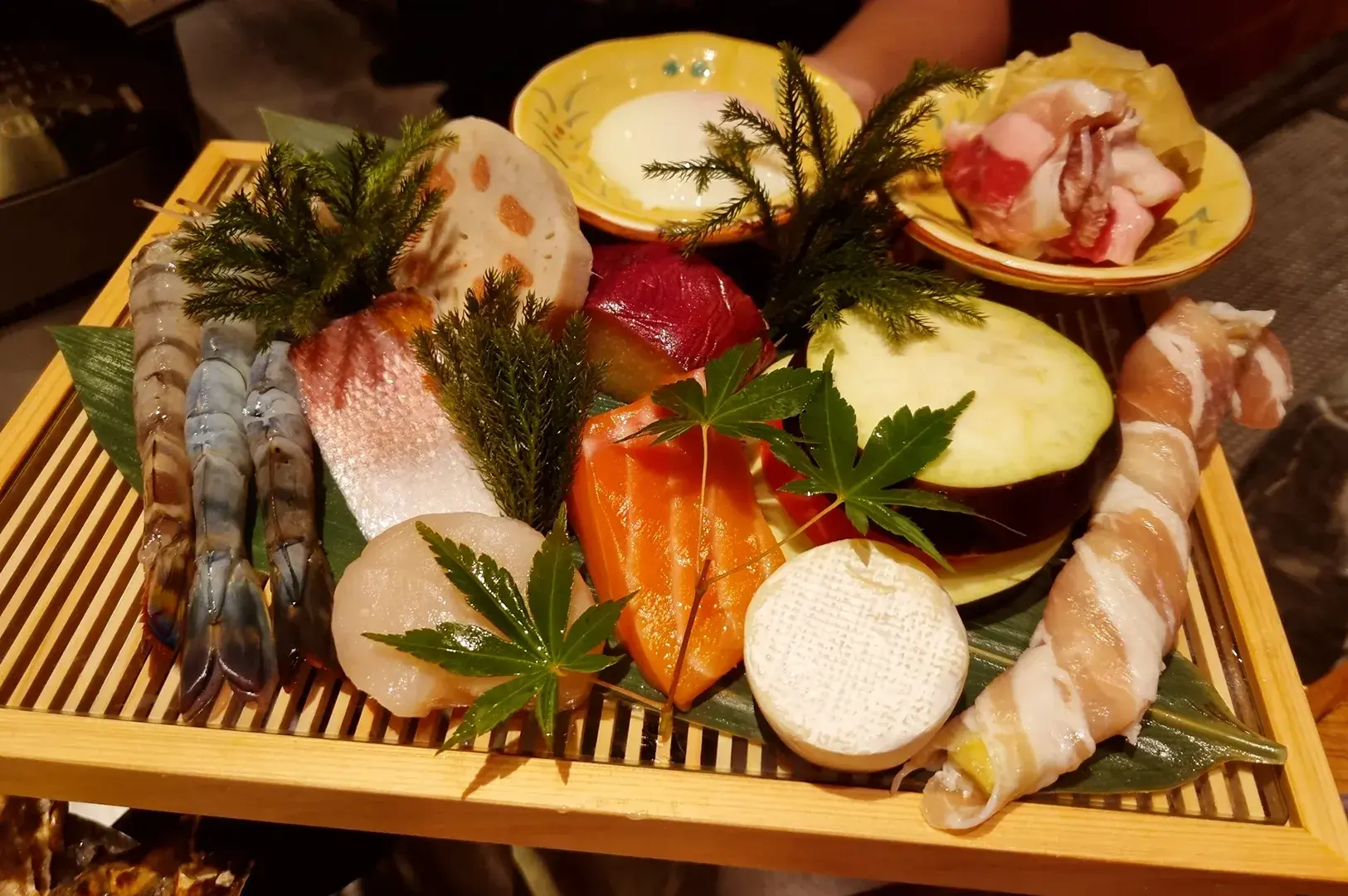 Assorted sashimi platter with shrimp, salmon, tuna, scallop, and garnish on a wooden tray.