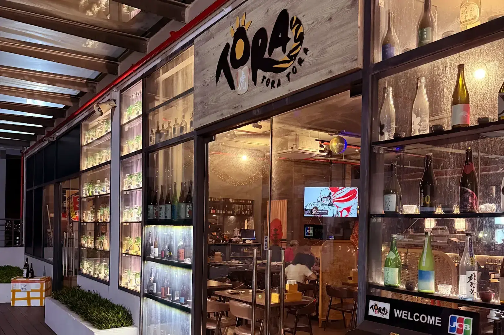 Tora Tora Tora restaurant entrance with illuminated bottle displays and dining area visible through glass doors.
