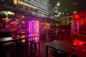 Kinki Restaurant + Bar’s outdoor dining area glowing with red and purple lights beneath the Fullerton Bay skyline at night.
