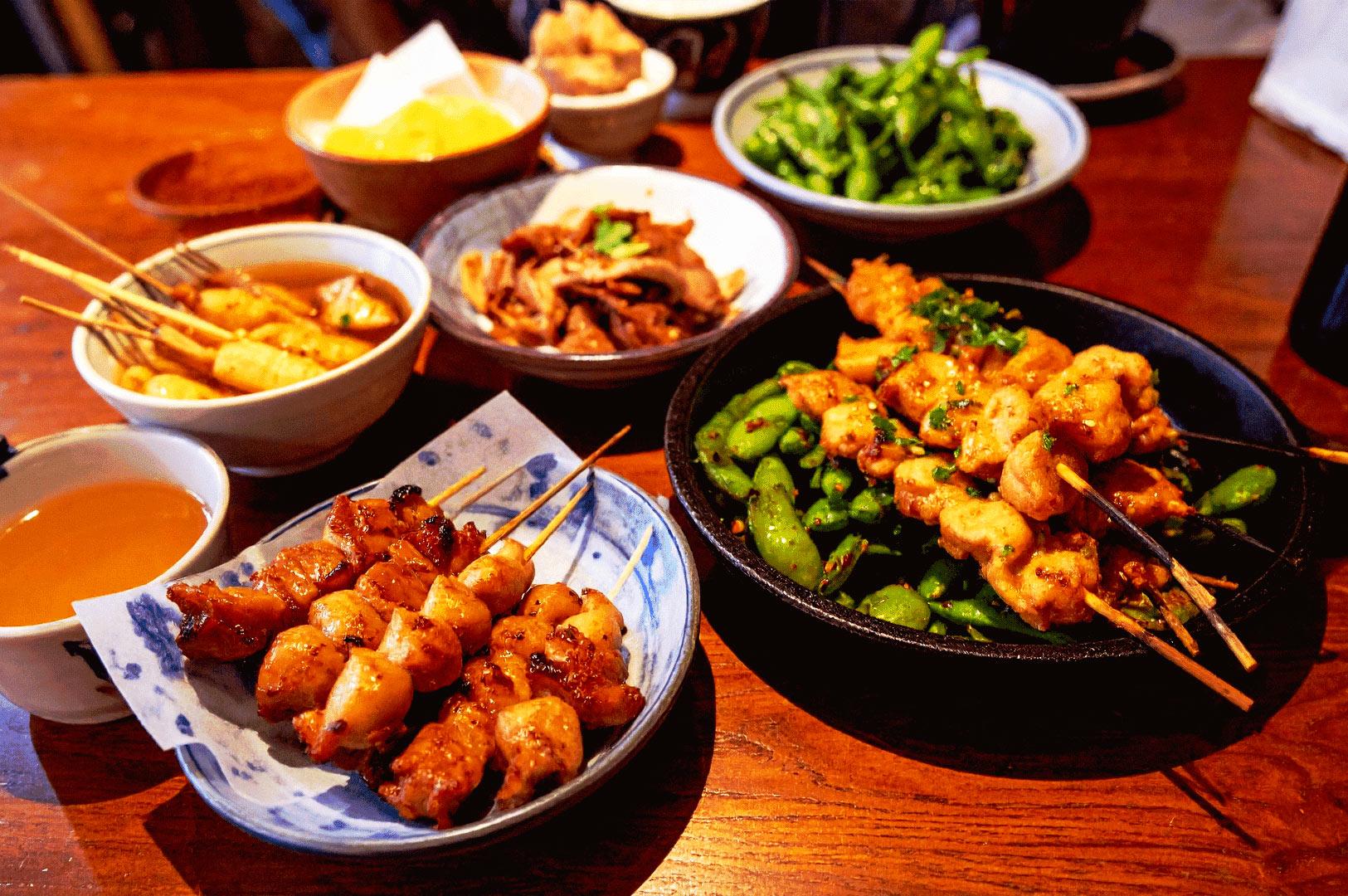 Japanese izakaya spread with grilled yakitori skewers, edamame, and small plates on wooden table in Singapore restaurant