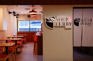 Soup Curry by Ki-setsu restaurant entrance with Japanese signage, red pendant lights, and an adjoining dining area with wooden tables and red chairs.