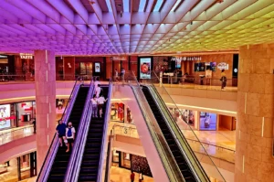 Vibrant multi-level ION Orchard interior with parallel escalators, illuminated storefronts, restaurants, shoppers, and a colourful geometric ceiling.