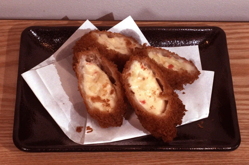 Breaded kani cream croquettes, split open to reveal a creamy filling, arranged on a black plate.