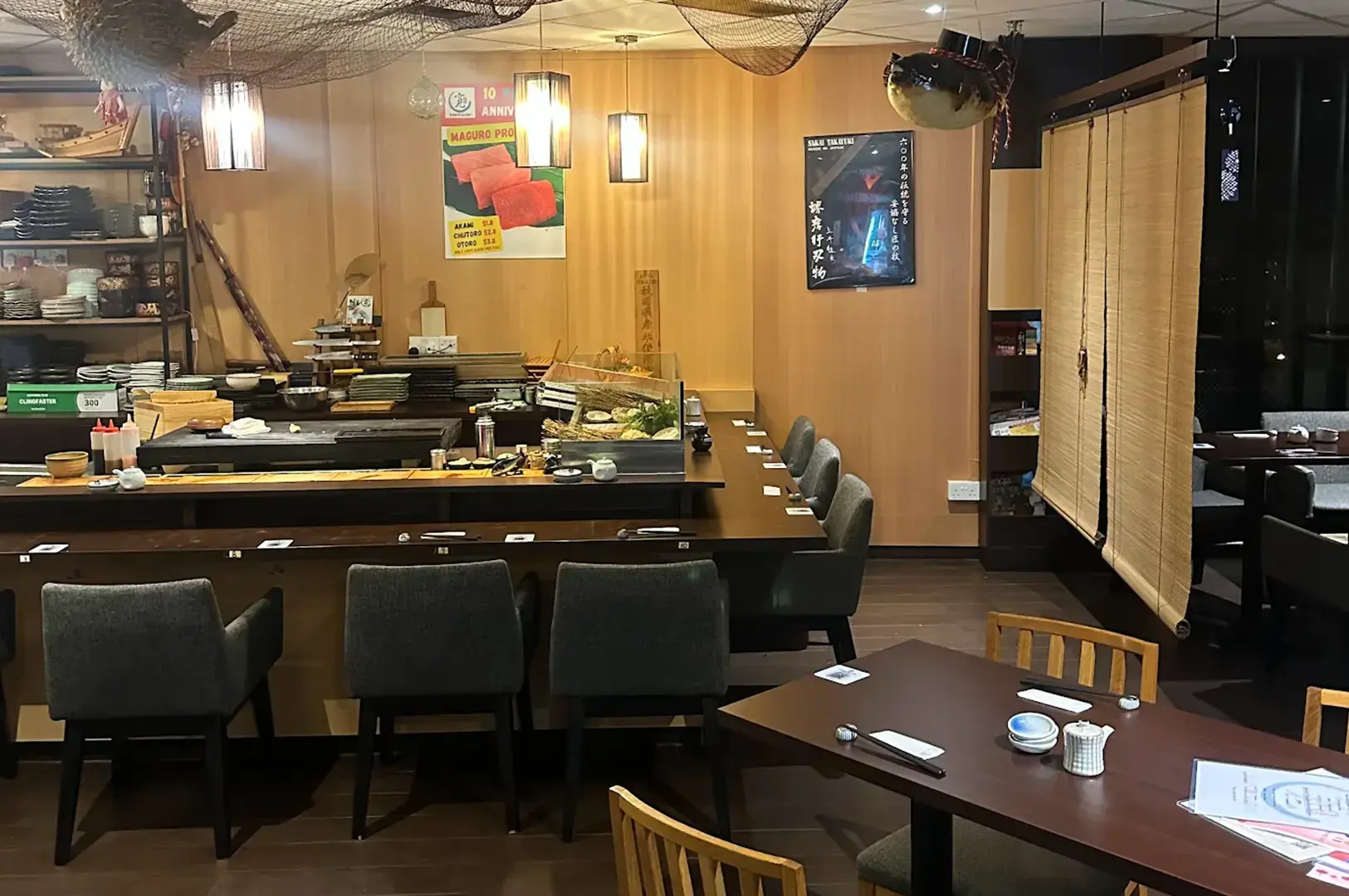 Interior of Kan Sushi Izakaya & Sake Bar showing the sushi counter, dining seats, wooden tables, Japanese artwork, and warm lighting.